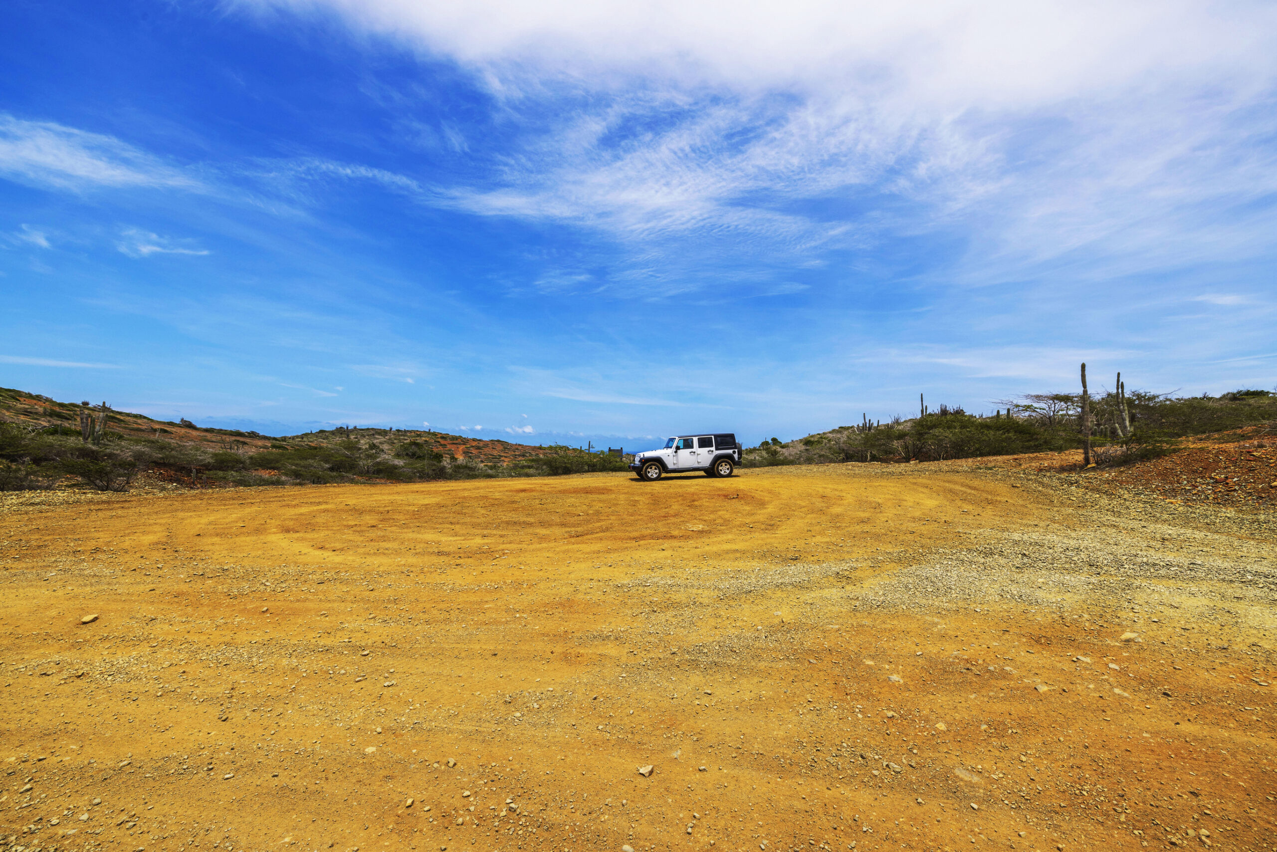 White Jeep on barren desert landscape under wide blue sky in Arikok National Park, Aruba. 