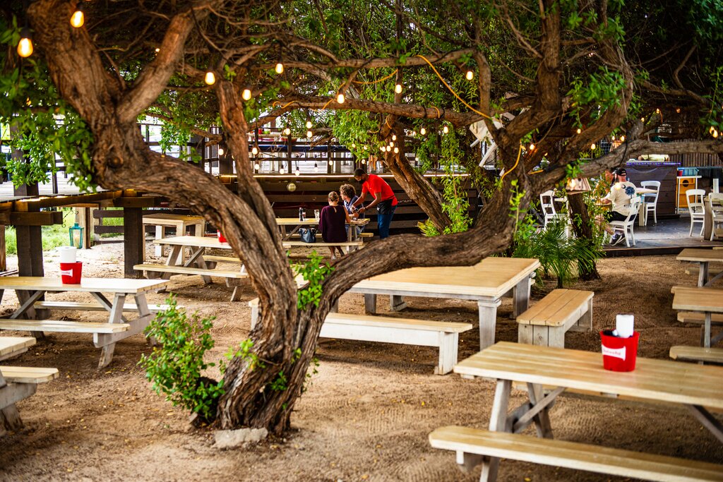 Outdoor picnic tables and tree at The West Deck Island Grill & Beach Bar.