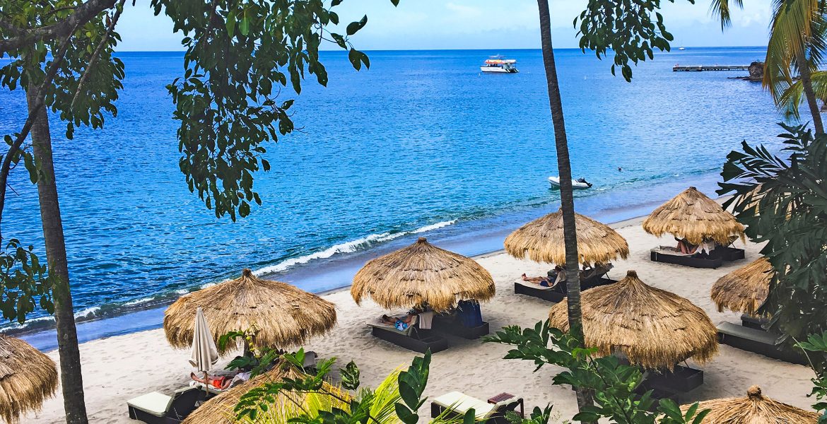 huts-on-beach-from-above-blue-water-green-palm-trees