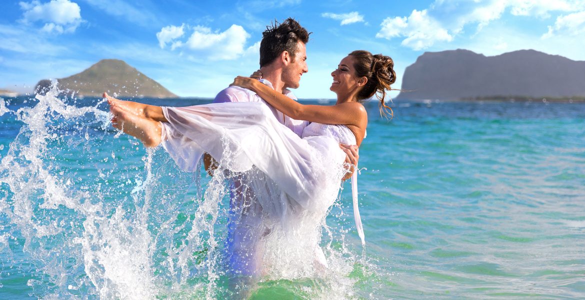 groom-holding-bride-in-clear-ocean-wearing-white