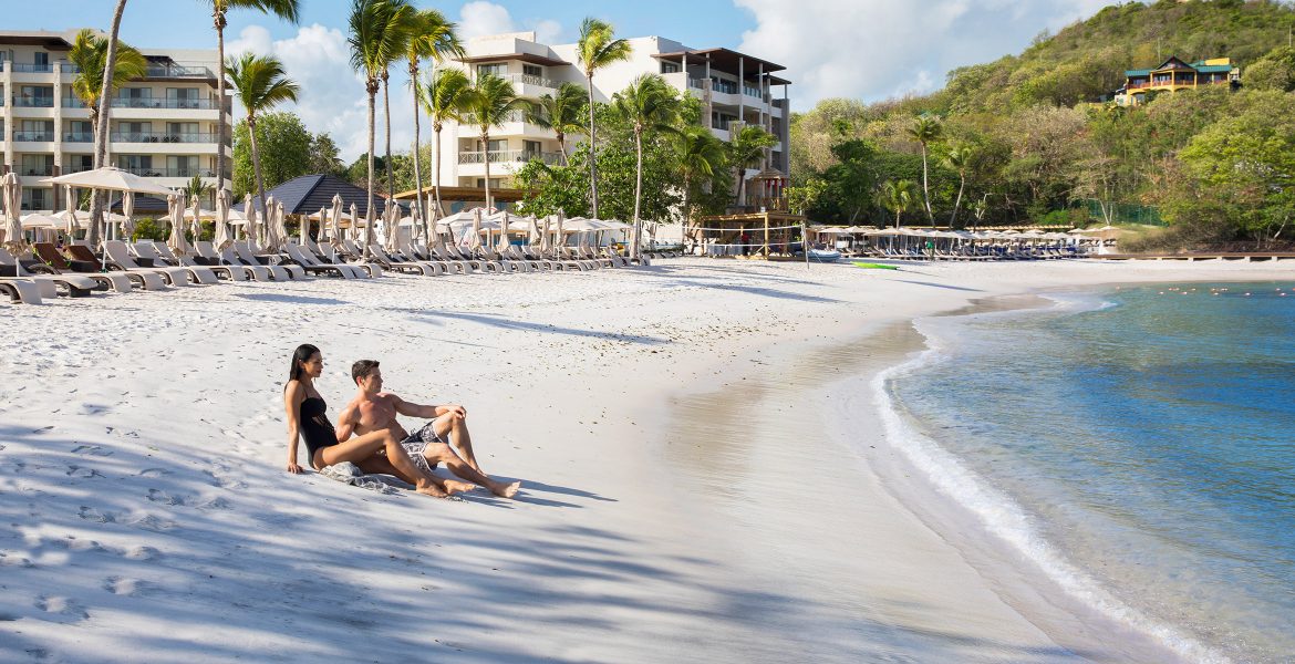 couple-sitting-white-sand-palm-trees-resort-background