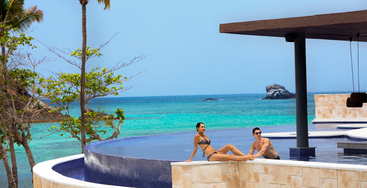 couple-sitting-private-infinity-pool-ocean-background
