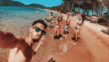guy-taking-selfie-of-him-and-friends-on-golden-sand-beach