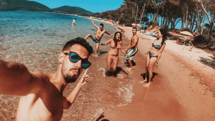 guy-taking-selfie-of-him-and-friends-on-golden-sand-beach