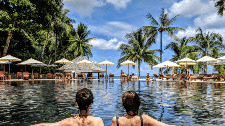 two-women-in-pool-looking-palm-tree-ocean