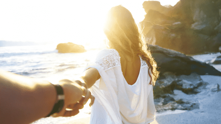 back-of-woman-holding-mans-hand-behind-her-beach