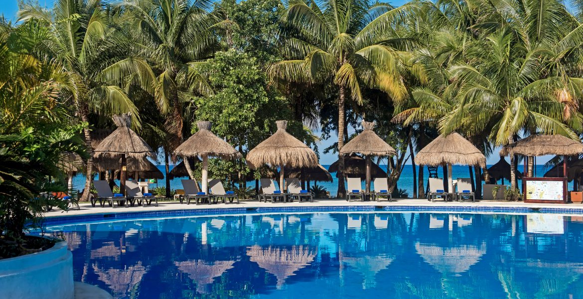 beach-resort-blue-pool-tiki-huts-loungers-green-palm-trees