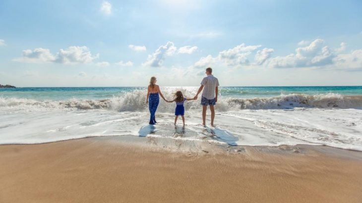 couple-holding-daughters-hands-waters-edge-beach-vacation