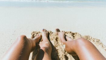 Two people dangle their legs on a rock by the beach