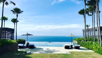 view-of-resort-infinity-pool-overlooking-ocean-palm-trees-buildings