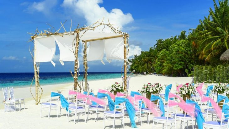 beach-wedding-set-up-chairs-archway-white-sand-blue-ocean-green-foliage