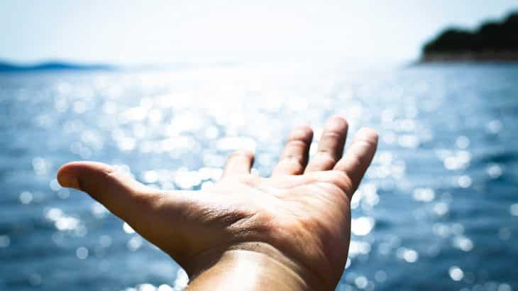 hand-reaching-out-over-ocean-sun-shining
