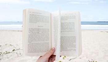 hand-holding-open-book-on-beach-sand-below