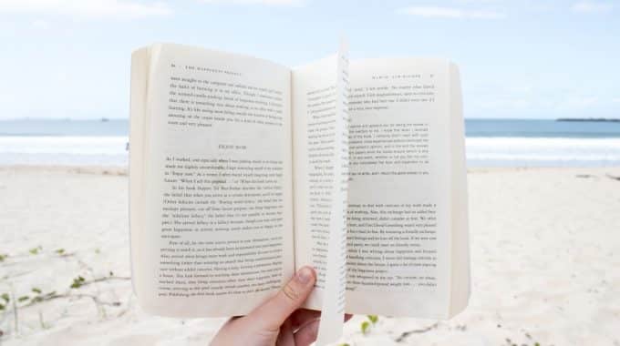 hand-holding-open-book-on-beach-sand-below