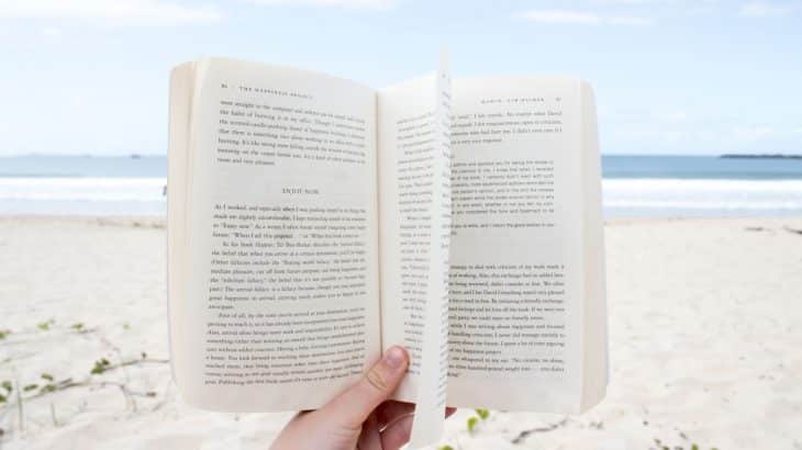 hand-holding-open-book-on-beach-sand-below