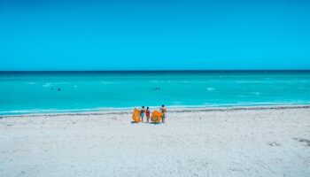 three-people-walking-on-beach-carrying-floats-to-ocean