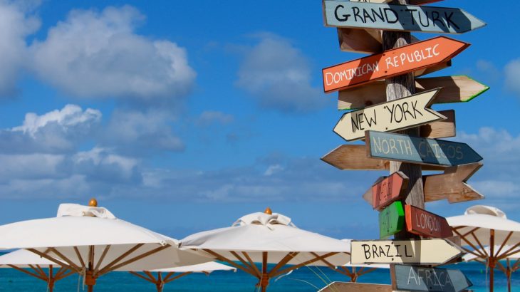 destinations-sign-on-beach-white-umbrellas-blue-sky-turks-caicos-islands