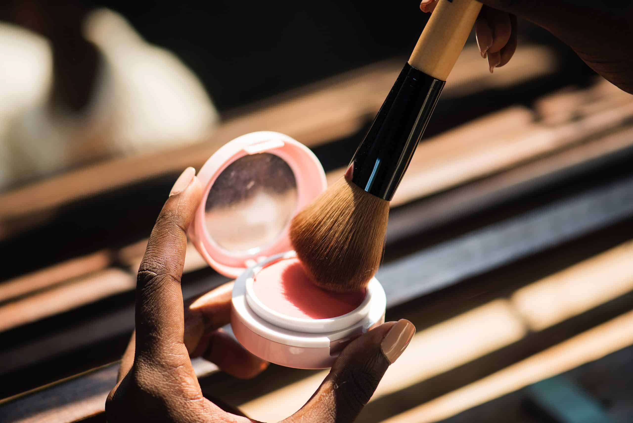 Someone dusts a makeup brush into a powder compact