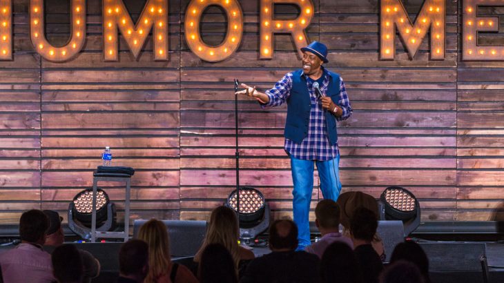 male-comedian-on-stage-in-front-of-sign-says-humor-me