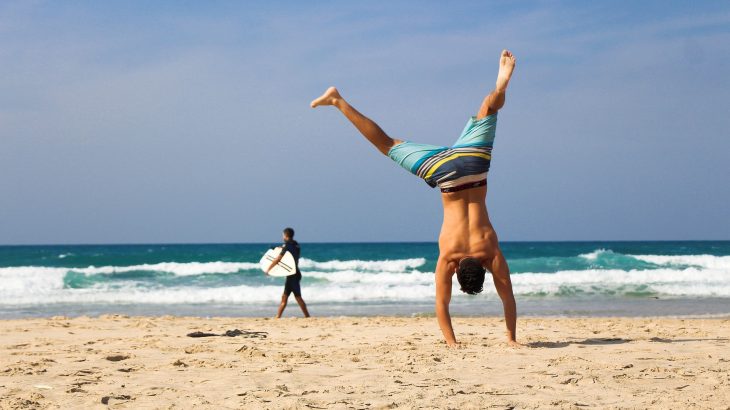 Man does cartwheel on beach in swimming trunks