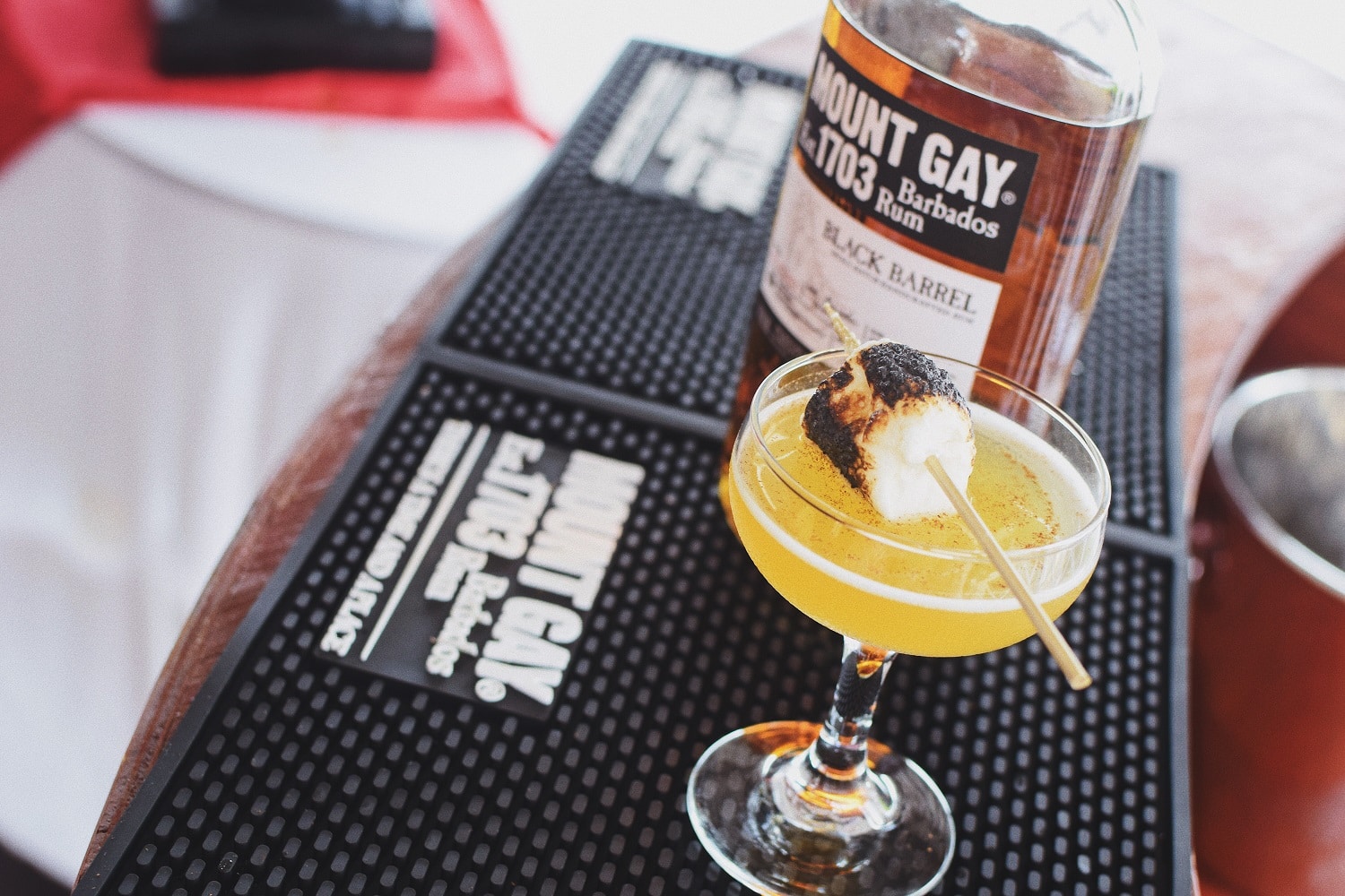 A craft cocktail topped with a seared marshmallow next to a bottle of Mount Gay rum