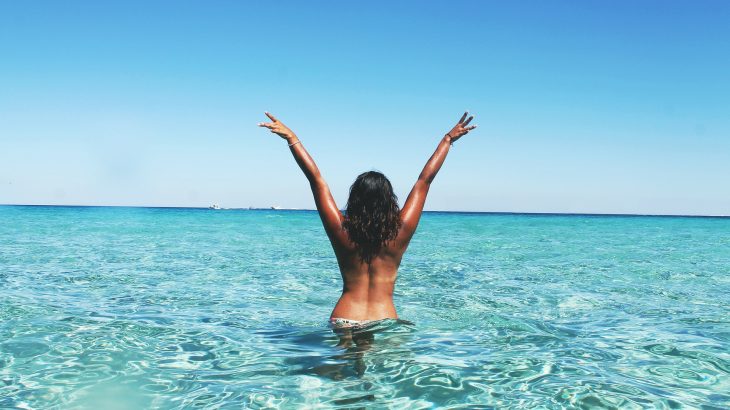 A girl throws her arms up in a bikini in the ocean