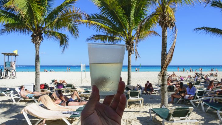 A person holding an alcoholic beverage in a plastic cup overlooking the beach