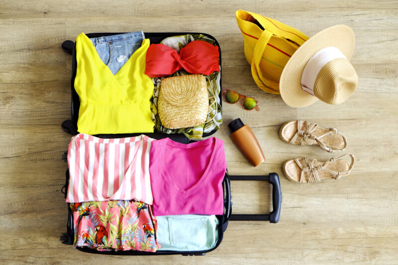 Open suitcase fully packed with folded women`s clothing and accessories on the floor.