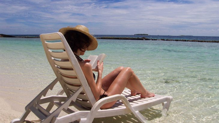 Woman sits on sun lounger in ocean reading book.