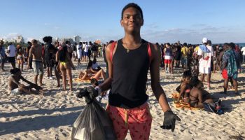 young boy picks up trash on busy Miami Beach