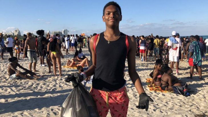 young boy picks up trash on busy Miami Beach