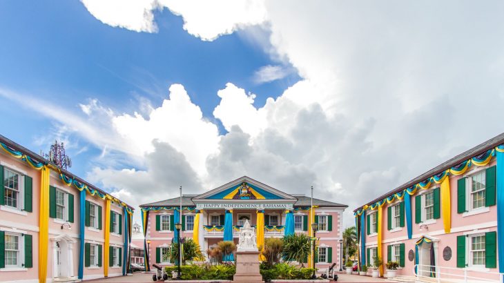 Three pink buildings with green shutters around a statue in Nassau, Bahamas