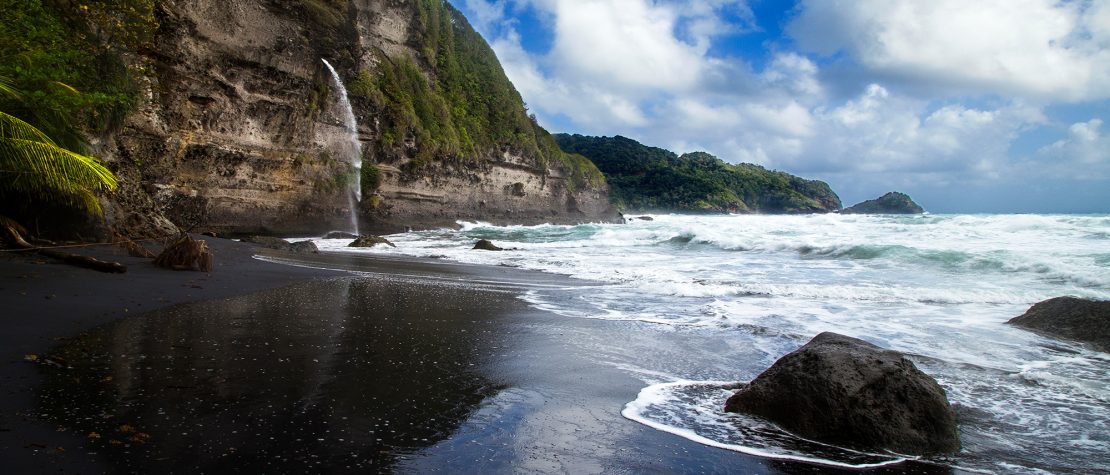 black sand beach in Dominica with huge cliffs