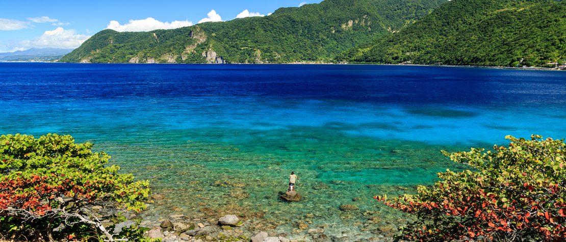 The ocean with a fisherman wading and mountains in the background