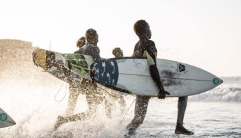 surfers in senegal running in water with surfboards at Copacabana Surf Village