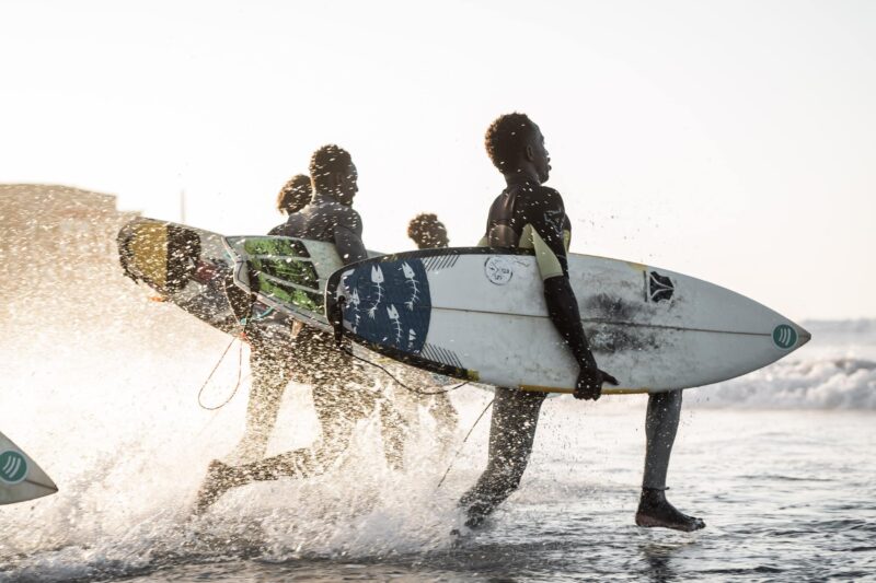 surfers in senegal running in water with surfboards at Copacabana Surf Village