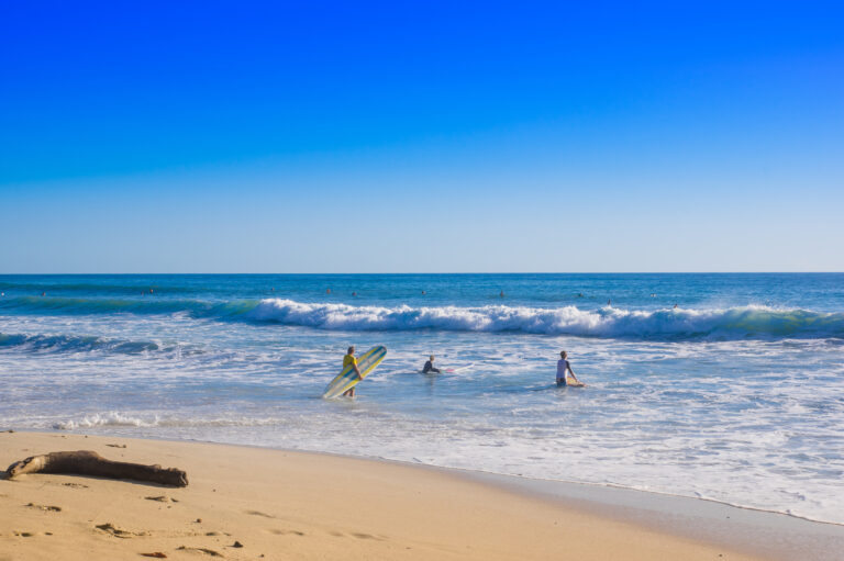 Outdoor view of surfers on the beach of Santa Teresa in a beautiful sunny day with blue sky and blue water in Costa Rica.