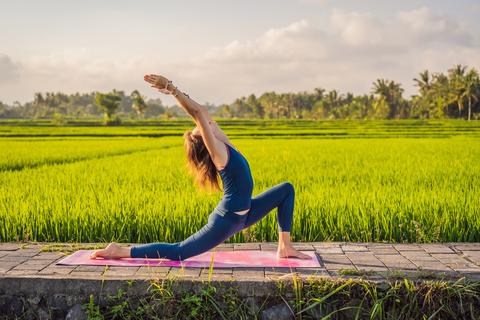 Young woman practice yoga outdoor in rice fields in the morning during wellness retreat in Bali.