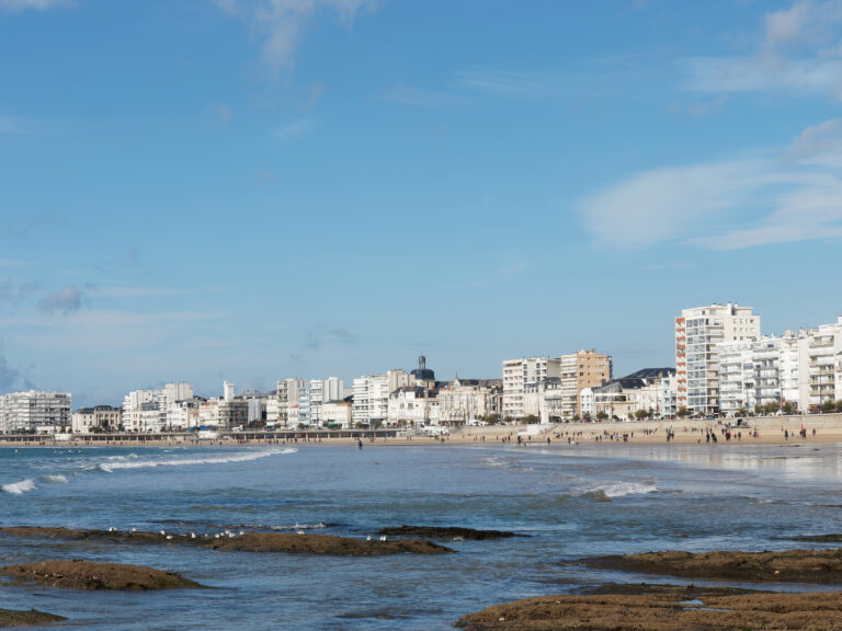 Les Sables d`Olonne, seafront a sunny day in autumn, white buildings and crescent form sand beach, France.