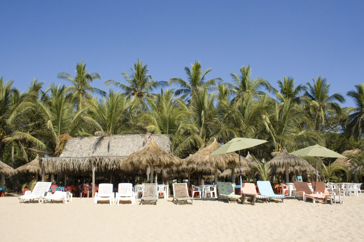 Sun loungers, shaded seating, a beach cafe and palm trees, on a beach in the village of San Francisco, otherwise known as San Pancho in Nayarit, Mexico