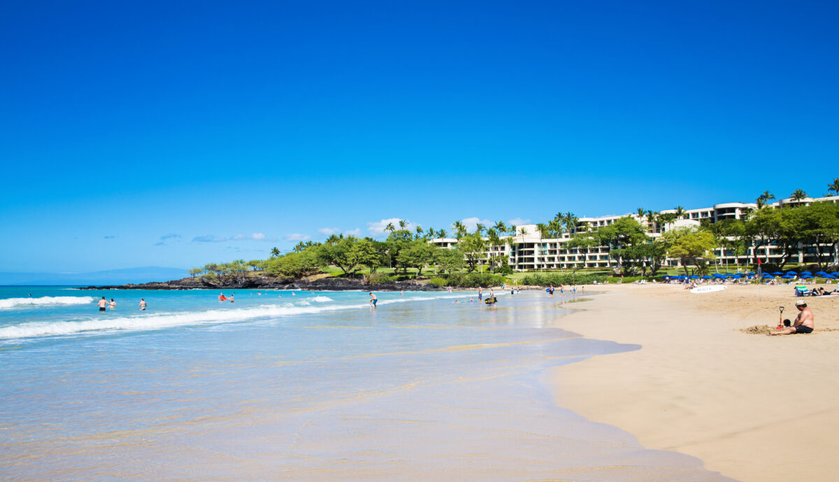 Tourist sunbathing and surfing on Mauna Kea Beach Big Island, Hawaii.