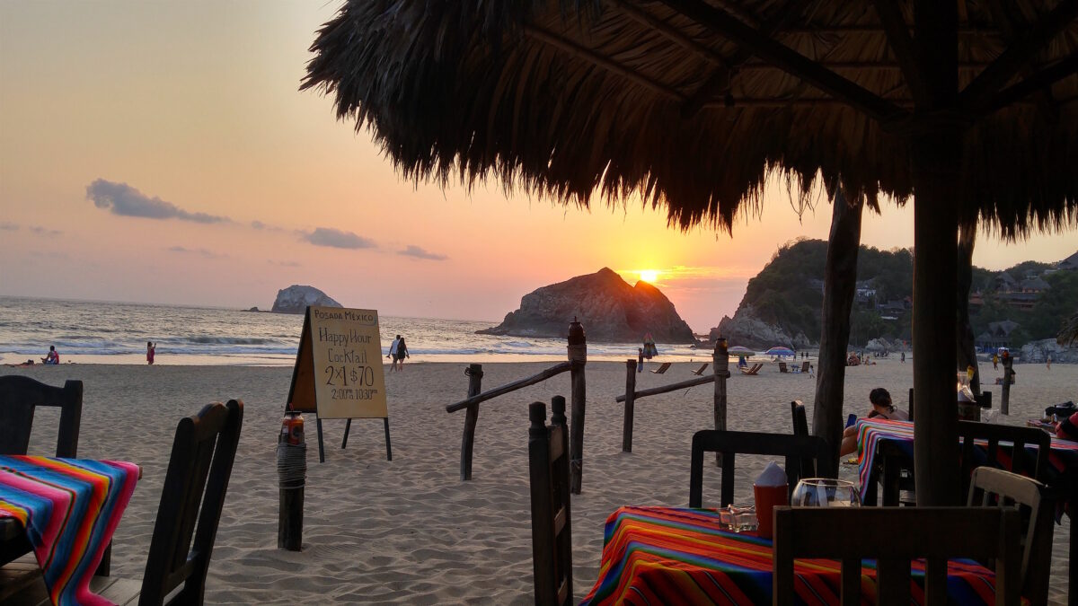The sun sets behind a rock in the Pacific Ocean on Zipolite Beach Playa Zipolite, Oaxaca, Mexico.