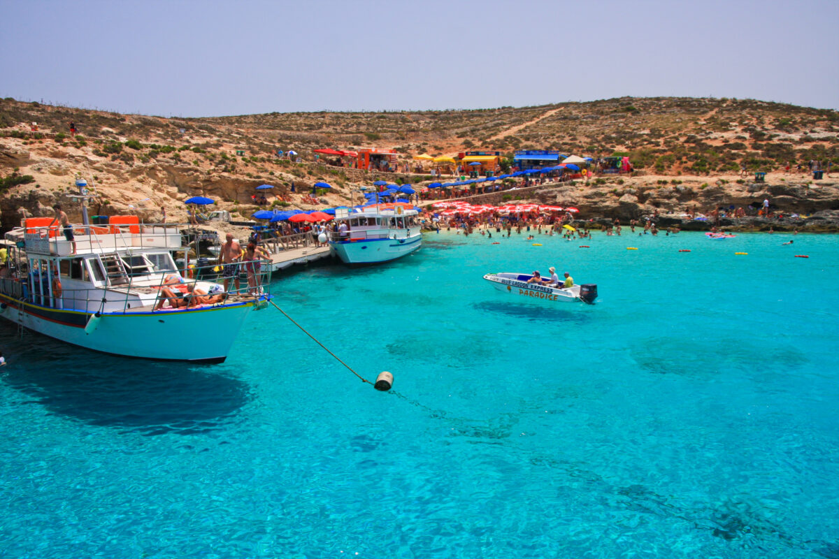 View of Blue Lagoon at Comino Island near Malta. Crystal clear sea water, cruise ships and people at beach.