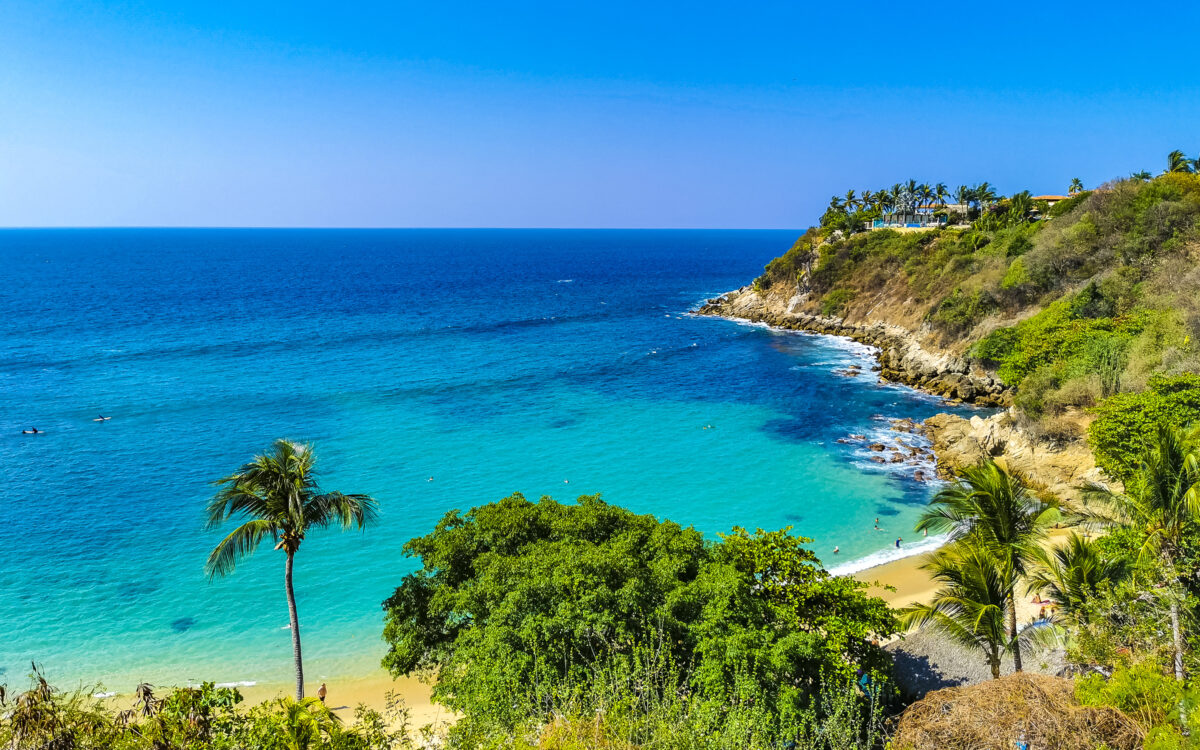 Beach sand turquoise blue water rocks cliffs boulders palm trees huge big surfer waves and panorama view on the beach Playa Carrizalillo in Puerto Escondido Oaxaca Mexico.
