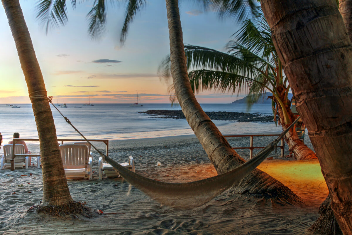 Sunset scene on Tamarindo beach in Costa Rica (Pacific ocean coast) featuring an empty hammock between two palm trees.