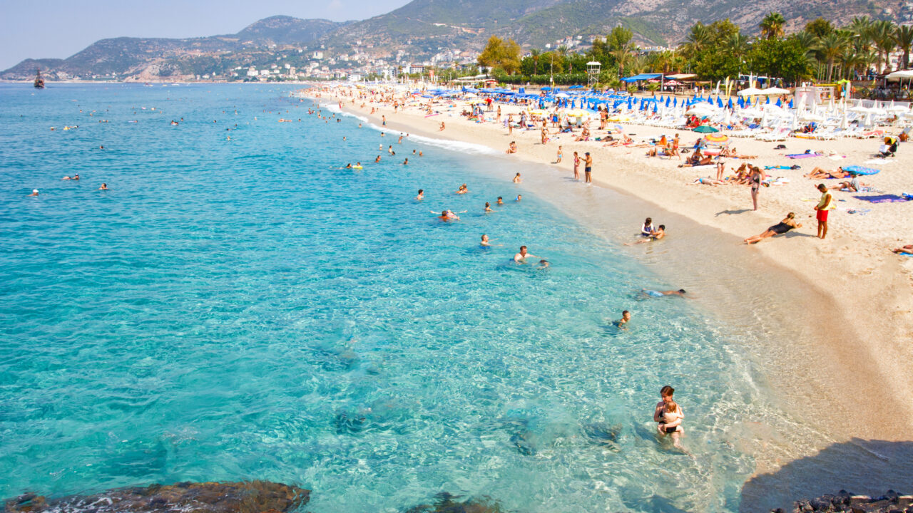 Tropical sea beach with swimming tourists on summer vacation resort.