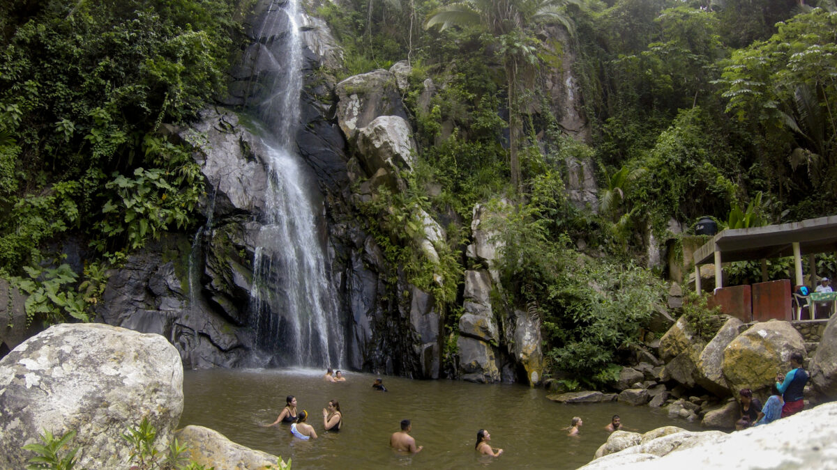 Waterfall in Yelapa, tropical beach tourists swimming under the waterfall during their vacation.