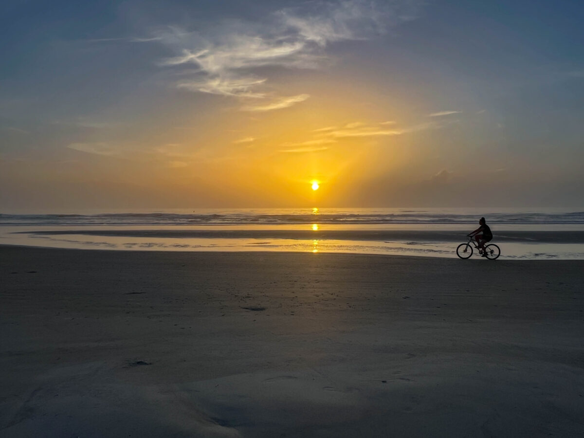 Person riding bike on beach at sunrise in New Smyrna Beach, FL.