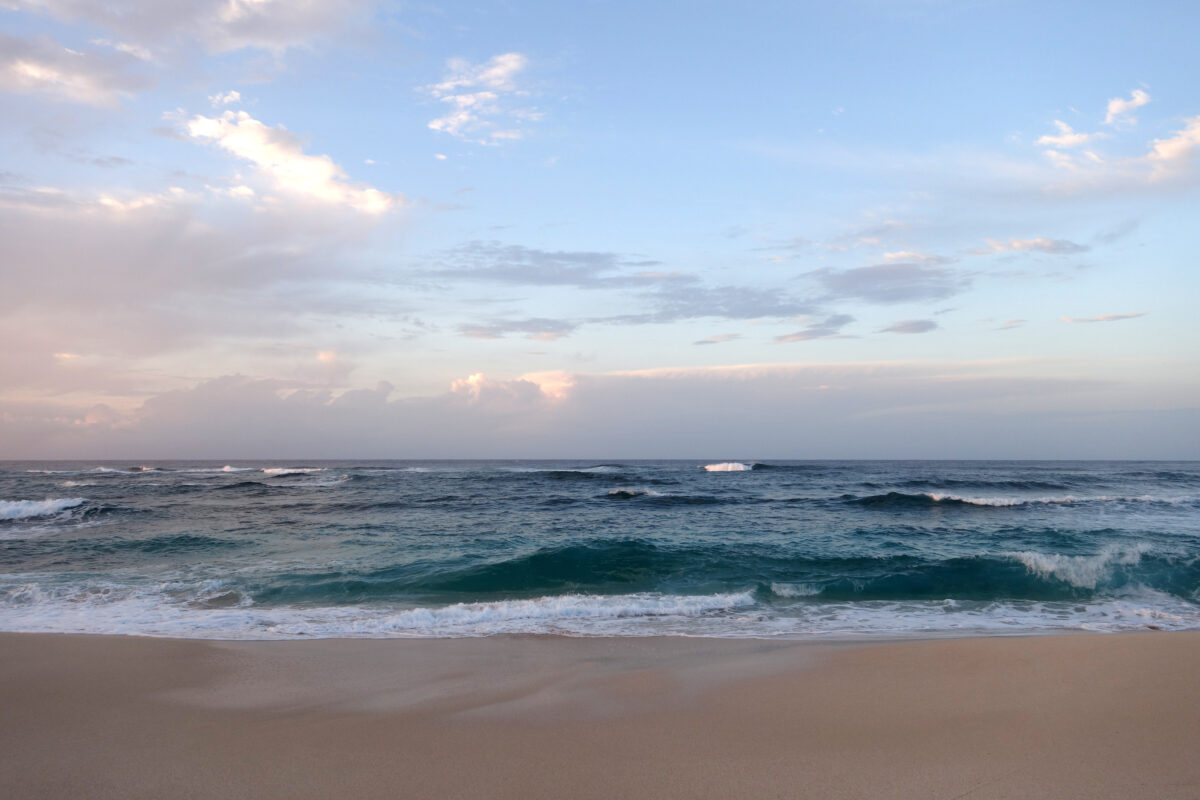 Waves break and crash towards the Hanakailio Beach with dramatic blue cloudy sky on the North Shore of Oahu, Hawaii.