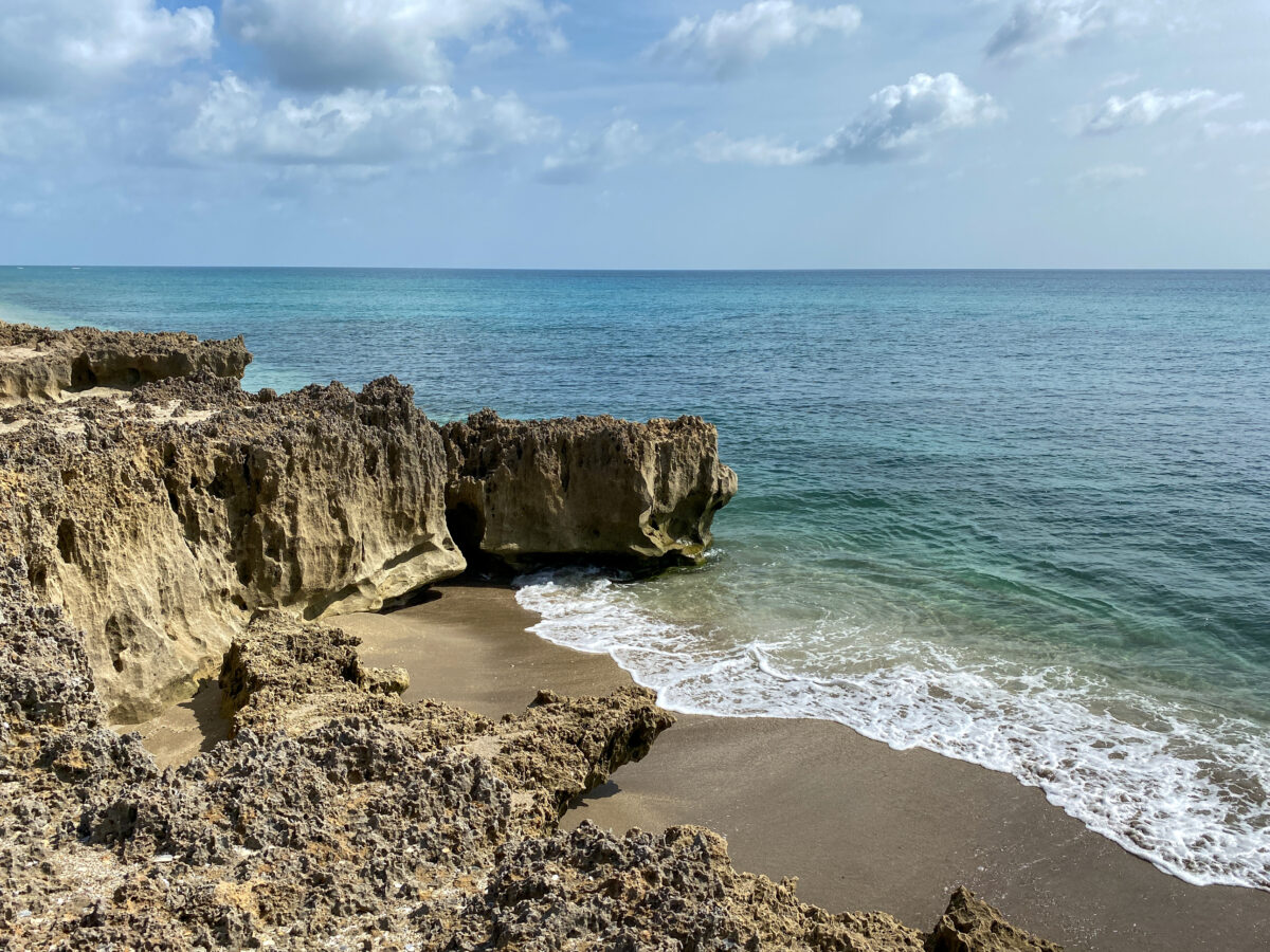 A rocky beach with clear turquoise water in Stuart, FL on a sunny day.